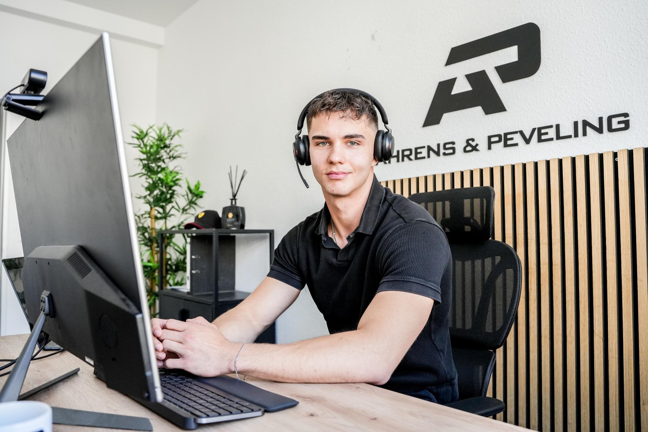 Kollege von Ahrens & Peveling mit Telefon-Headset am Schreibtisch, im Hintergrund das AP-Logo an der Wand.