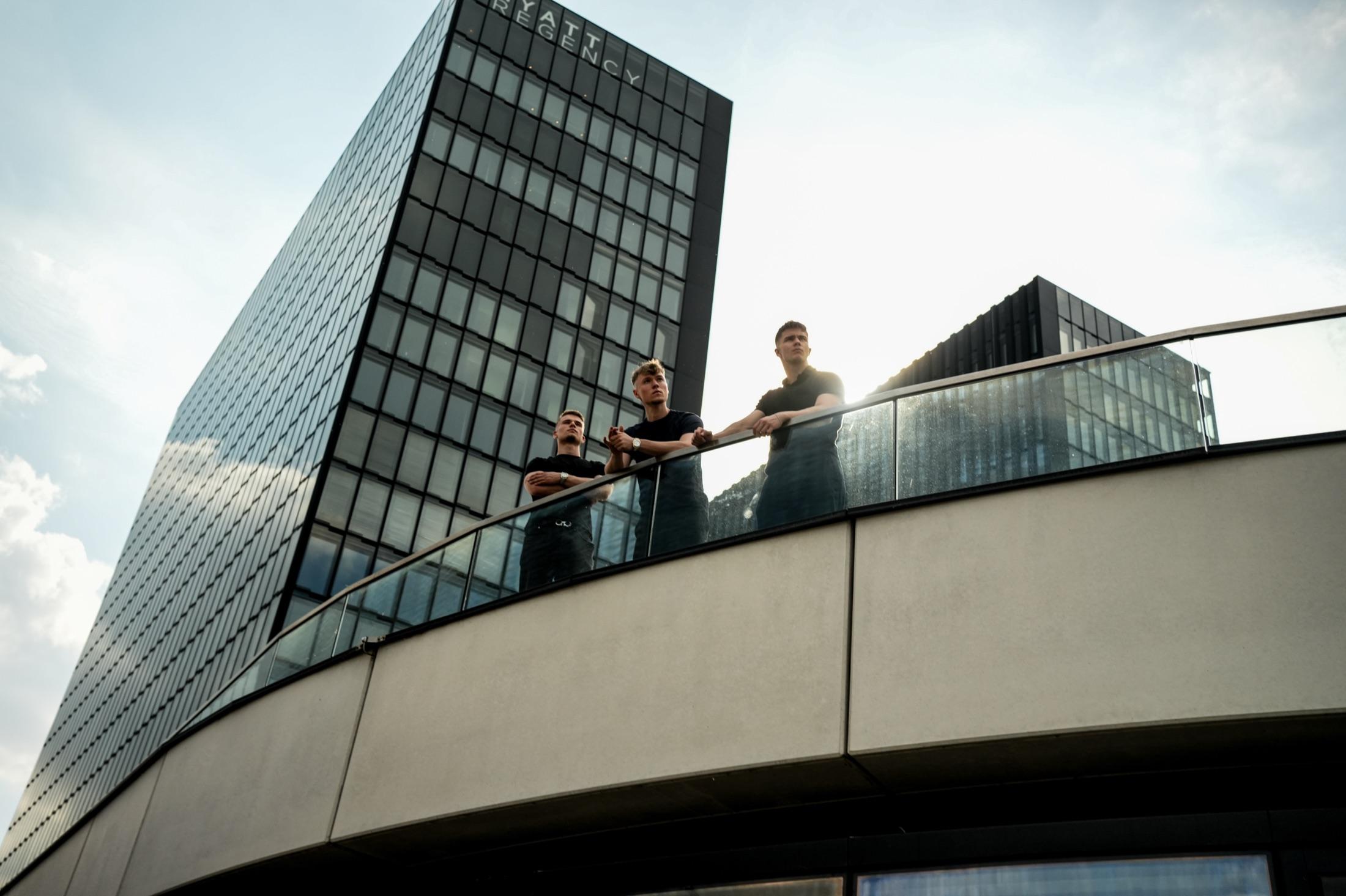 Drei Kollegen von Ahrens & Peveling stehen zusammen auf der Dachterrasse vor dem Bürogebäude.